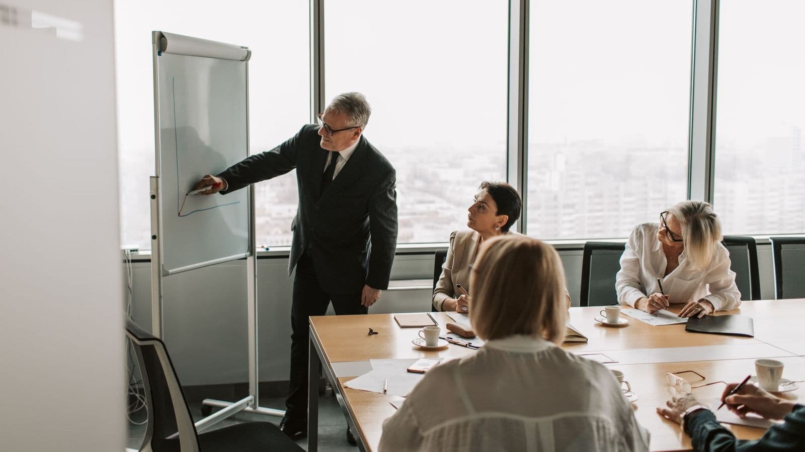 A senior executive presenting at a whiteboard to colleagues in a boardroom
