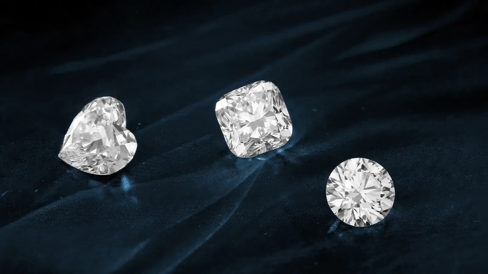 Three loose diamonds in heart, cushion and round cuts on dark fabric