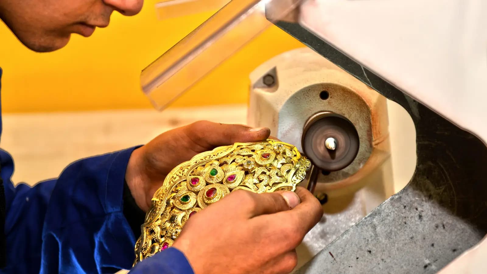 Craftsman polishing an ornate gold piece set with red and green stones