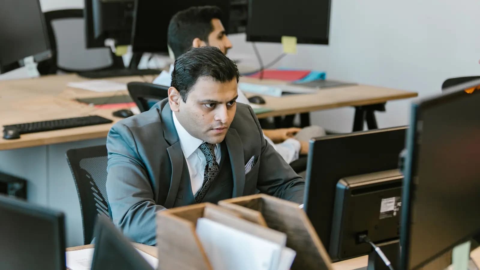 Office worker in a suit at a computer in an open plan office