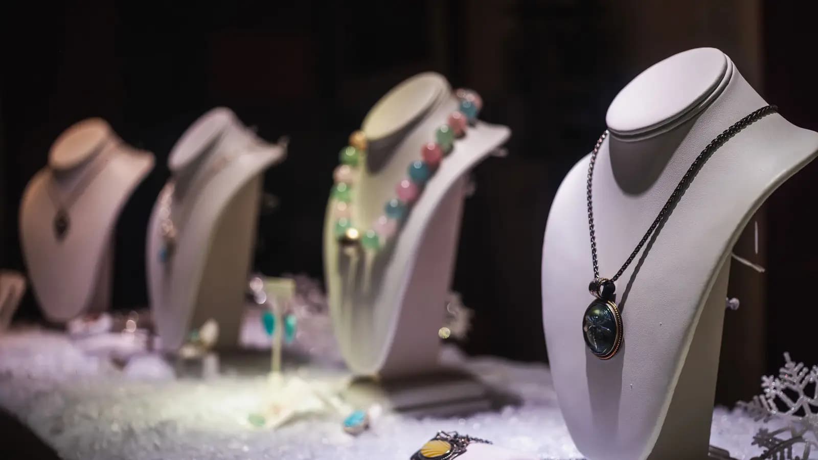 Necklaces and pendants arranged on white display busts in a lit jewellery window