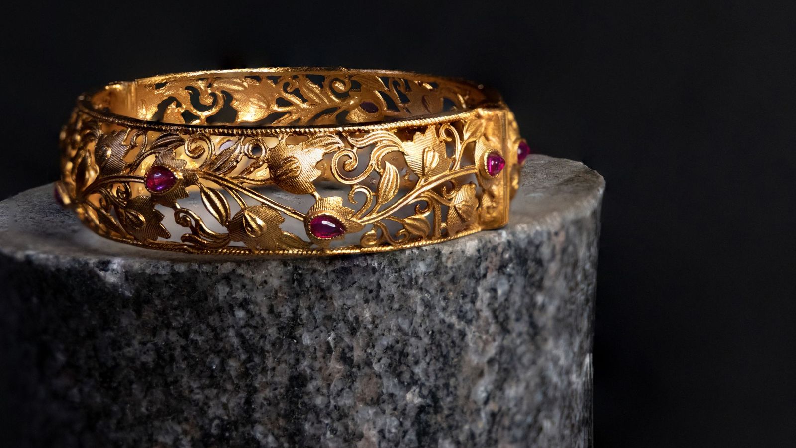 An engraved gold bangle set with rubies on a stone plinth