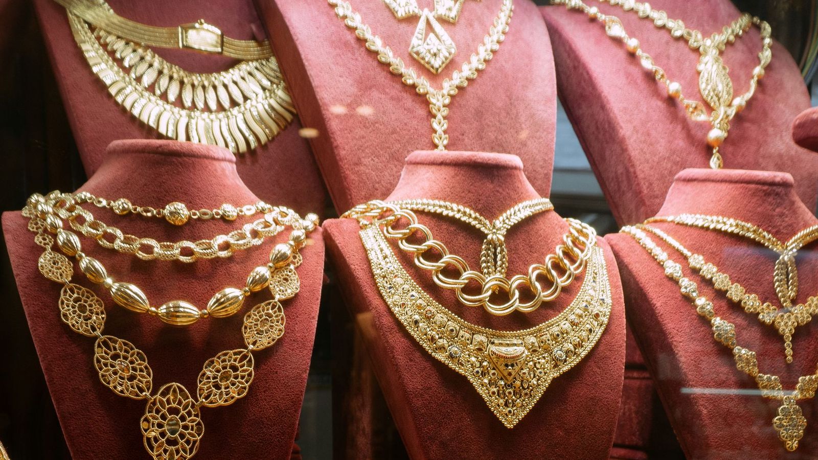 Gold necklaces displayed on red busts in a gold market window