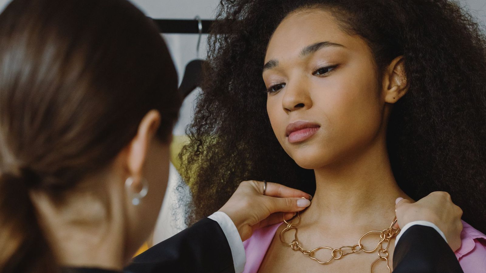 A stylist fastening a gold necklace on a customer in a store